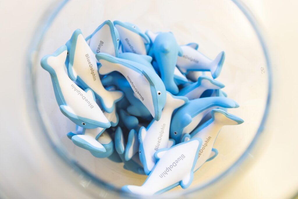 Blue and white BlueDolphin-branded foam dolphin stress toys collected inside a clear glass bowl.