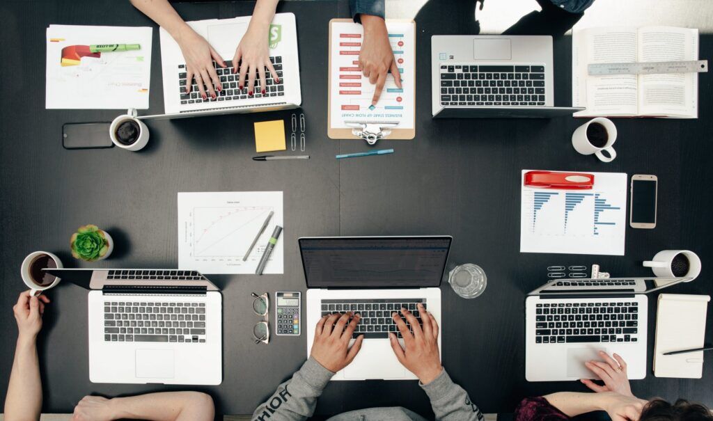 Overhead view of a team working on laptops around a dark desk with charts, coffee cups, and business documents.