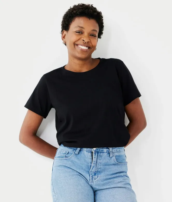 Smiling woman with short curly hair wearing a black t-shirt and light blue jeans against a white background.
