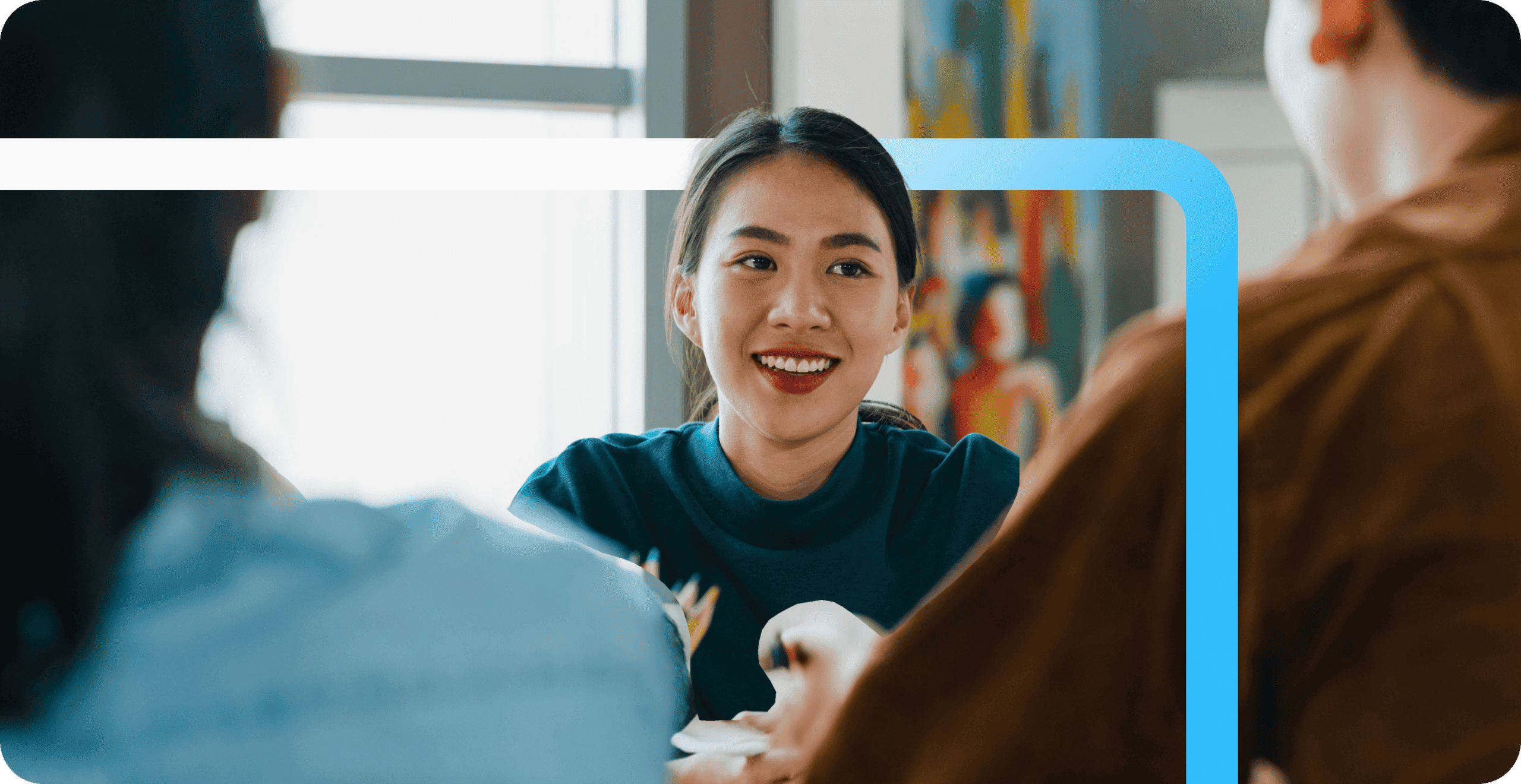 A smiling young woman in a teal shirt engages in conversation with colleagues at a Randstad center.