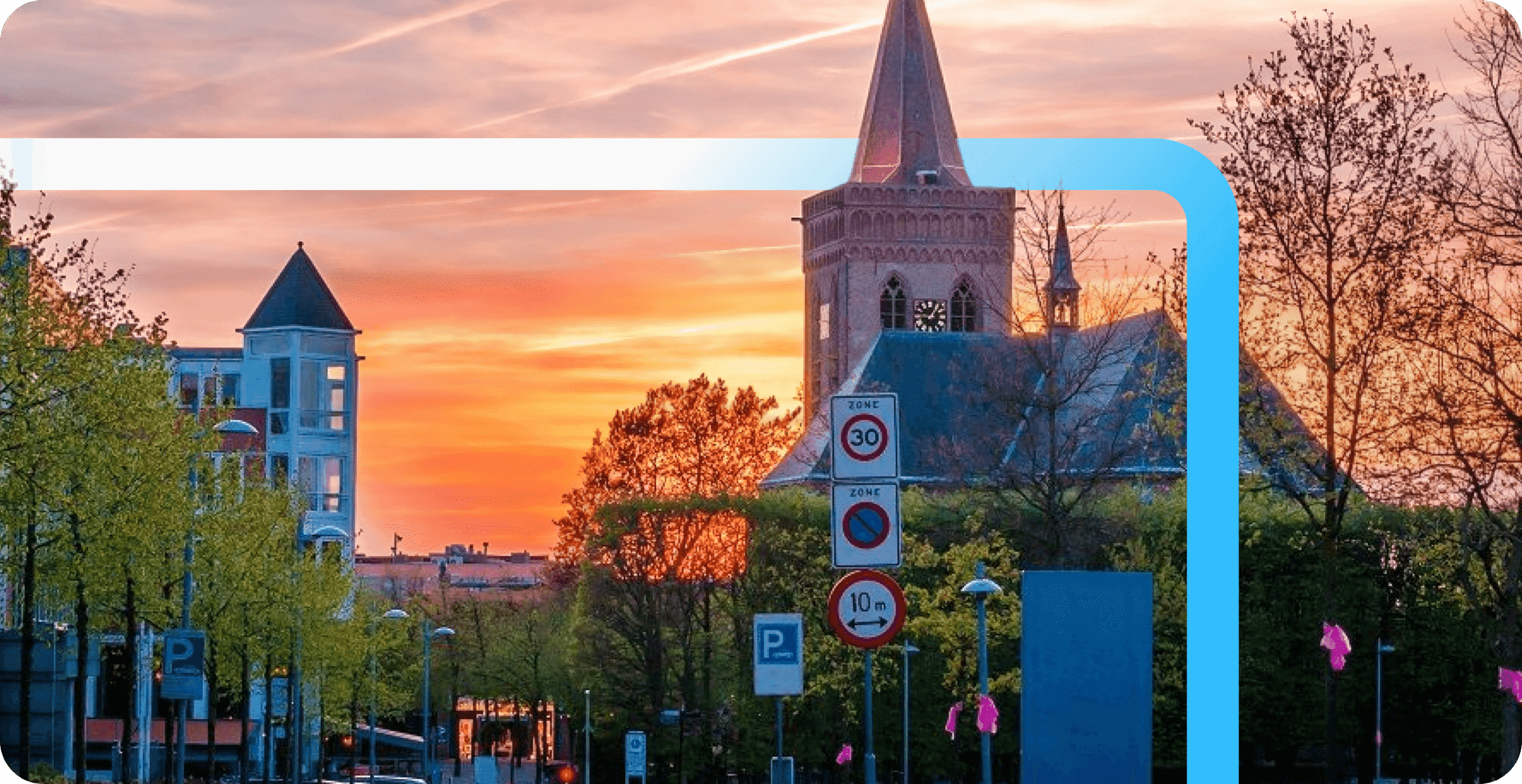 European town center at sunset with a historic church tower, tree-lined streets, and traffic signs against a vibrant orange