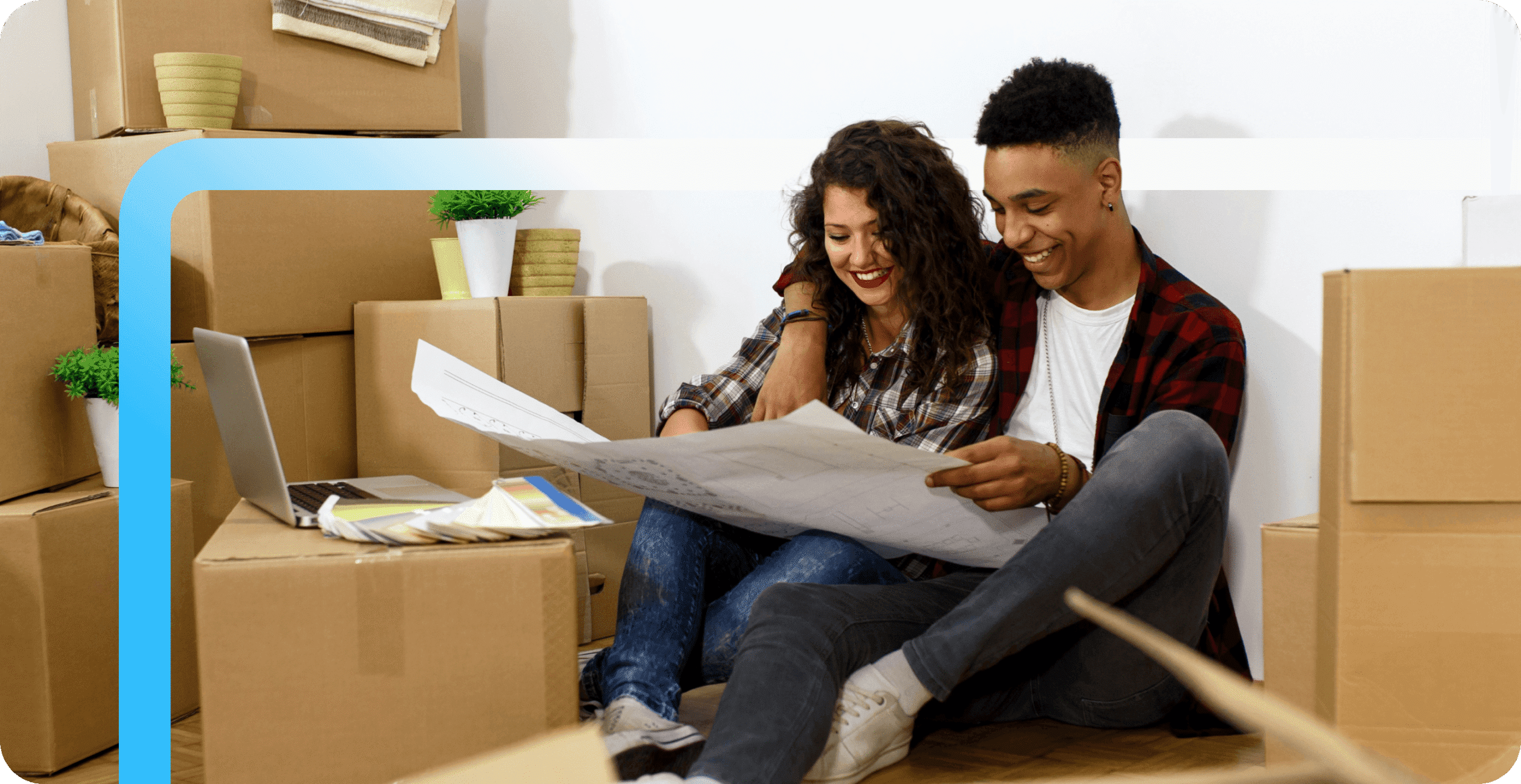 A smiling young couple sits on the floor surrounded by moving boxes, reviewing documents together in their new home.