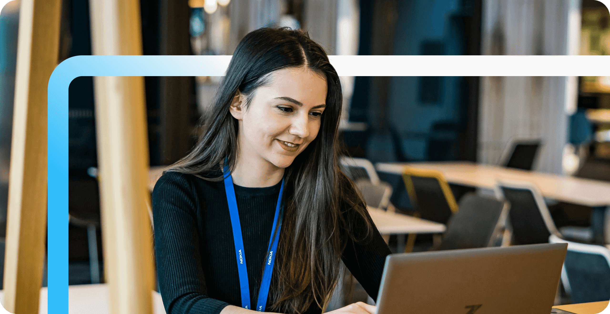 A smiling woman wearing a Nokia lanyard works on a laptop in a modern office environment.