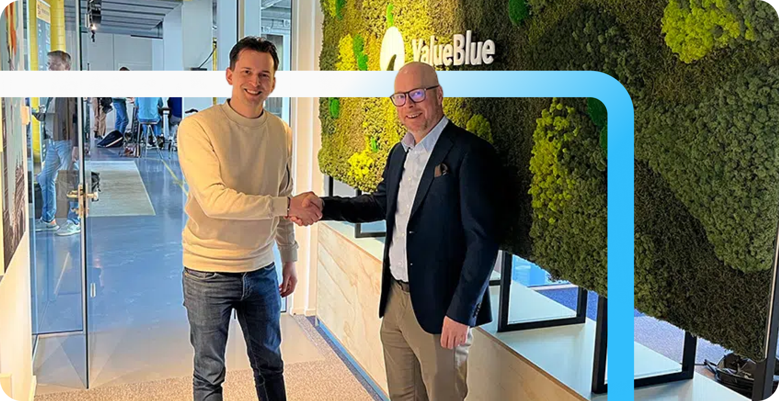Two men shaking hands and smiling in front of a green moss wall with the ValueBlue logo at a modern office.
