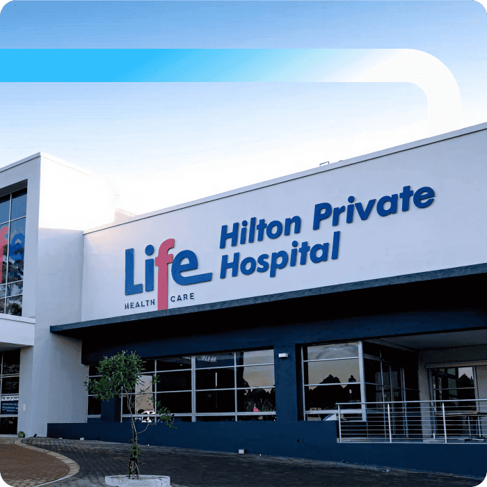 Exterior of Life Healthcare Hilton Private Hospital, a modern white building with blue signage and a paved entrance area.