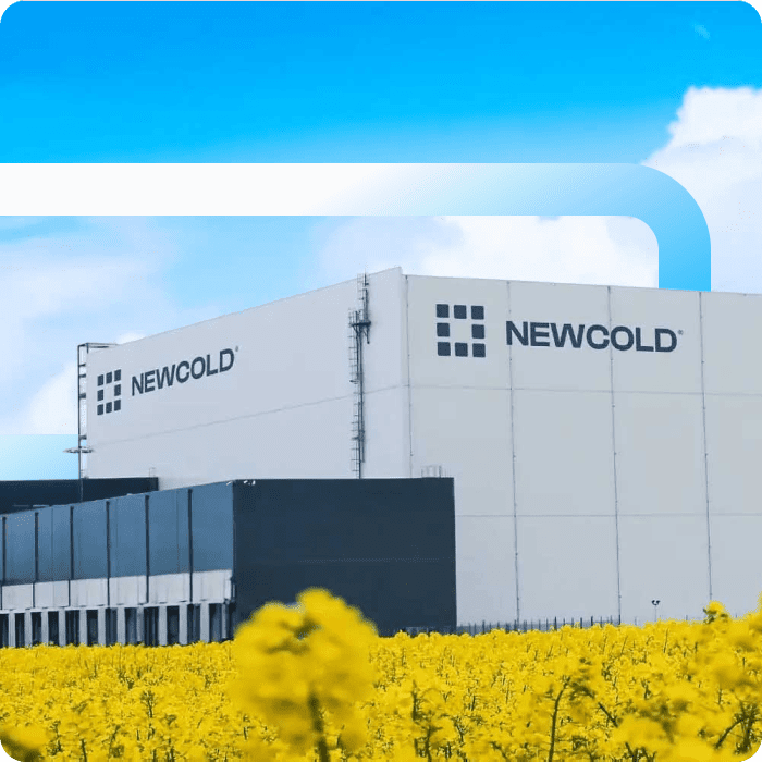 Large white NewCold cold storage warehouse facility with branded signage surrounded by a bright yellow rapeseed field under