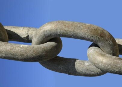 Close-up of heavy, weathered metal chain links interlocked against a clear blue sky.