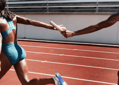 Two female relay runners passing a baton on a red track, symbolizing teamwork and collaboration.