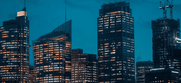 Skyscrapers with illuminated windows stand against a blue evening sky in a cityscape.