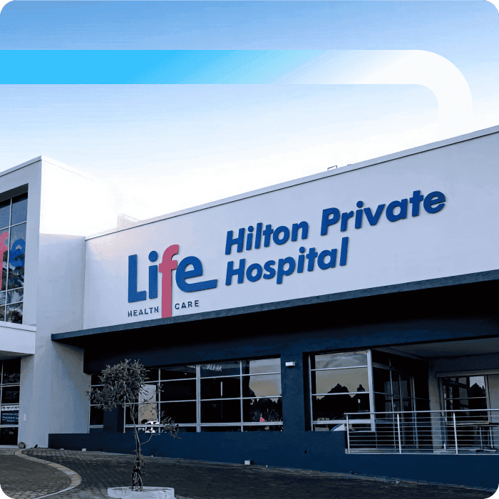 Exterior of Life Healthcare Hilton Private Hospital, a modern white building with blue signage and a paved entrance area.