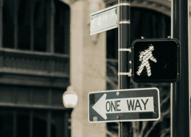 A lit walk signal, a one way sign, and an E 4th St street sign at a city intersection.