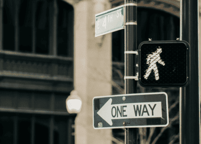 A lit walk signal, a one way sign, and an E 4th St street sign at a city intersection.